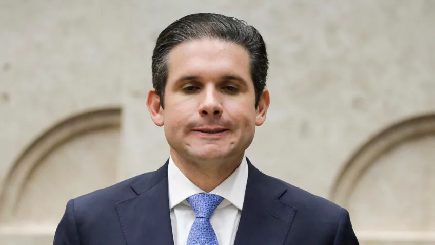 Retrato em close do Deputado Hugo Motta (Republicanos-PB), Presidente da Câmara, ligado a denúncias de rachadinha e violência contra jornalistas no plenário.